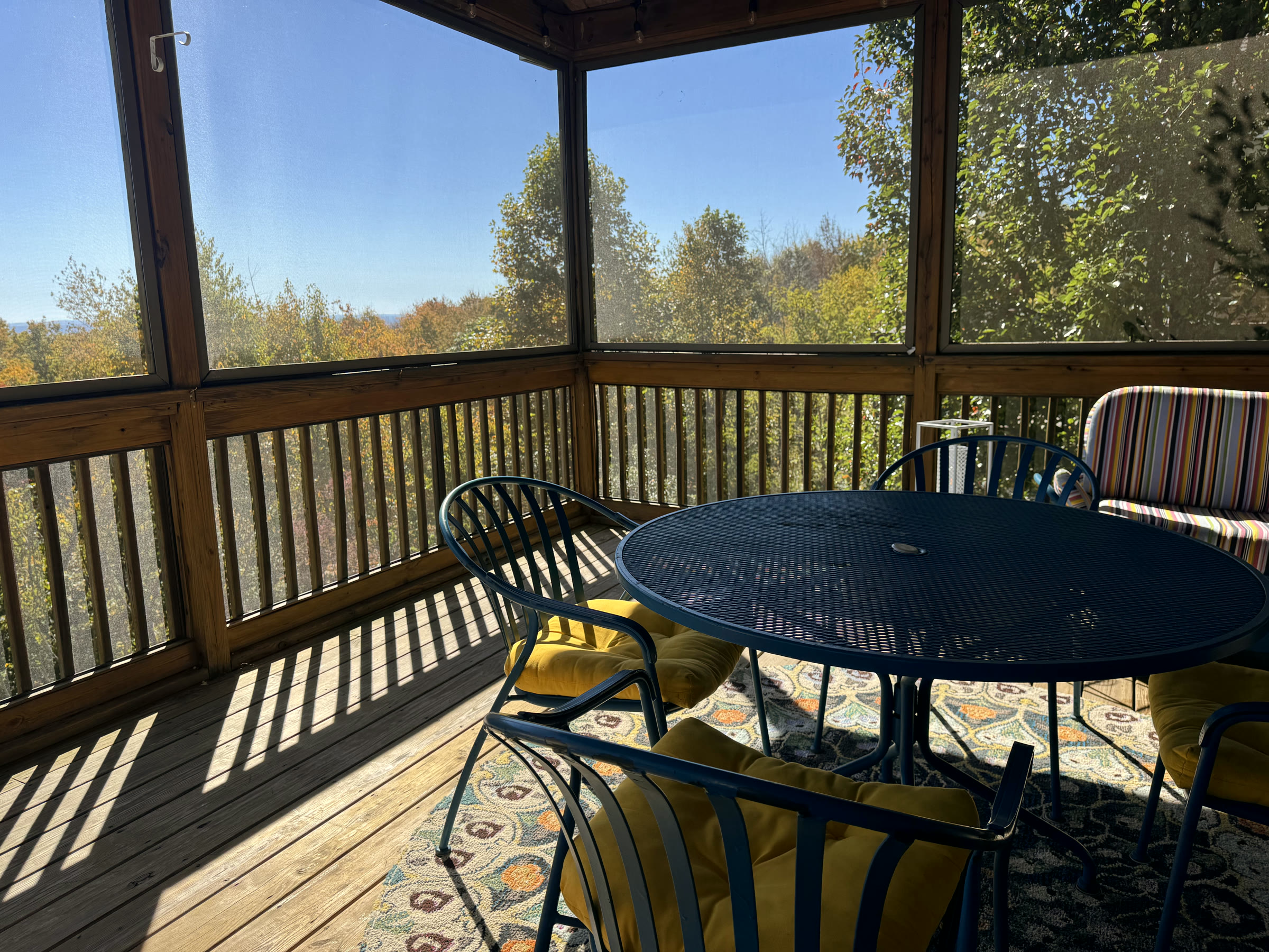 The covered porch at South Ridge with a table and chairs, trees turning beyond